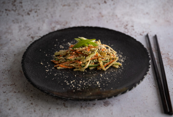 Vegetarian kani salad made with hearts of palm marinated in dill, lemon juice, and nori flakes, served with julienned carrots and cucumbers, topped with sesame seeds and spring onions.